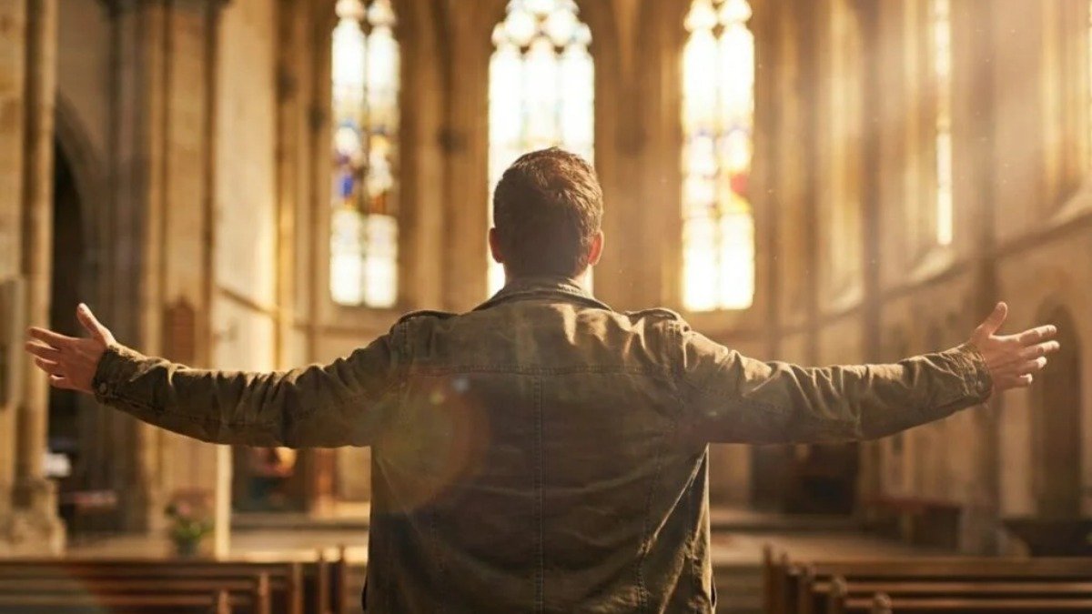 Pessoa em adoracao com bracos levantados em igreja iluminada pela luz do Espirito Santo