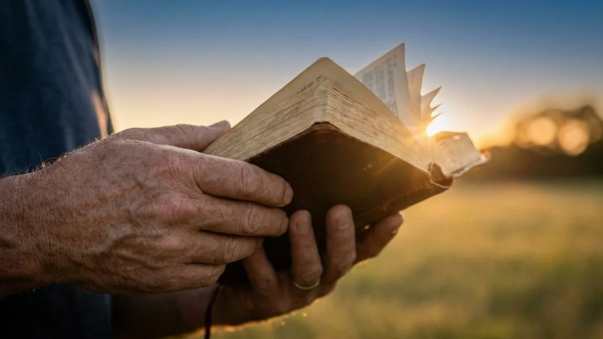 Maos segurando uma Biblia aberta ao ar livre durante o por do sol, luz dourada simbolizando a presenca do Espirito Santo